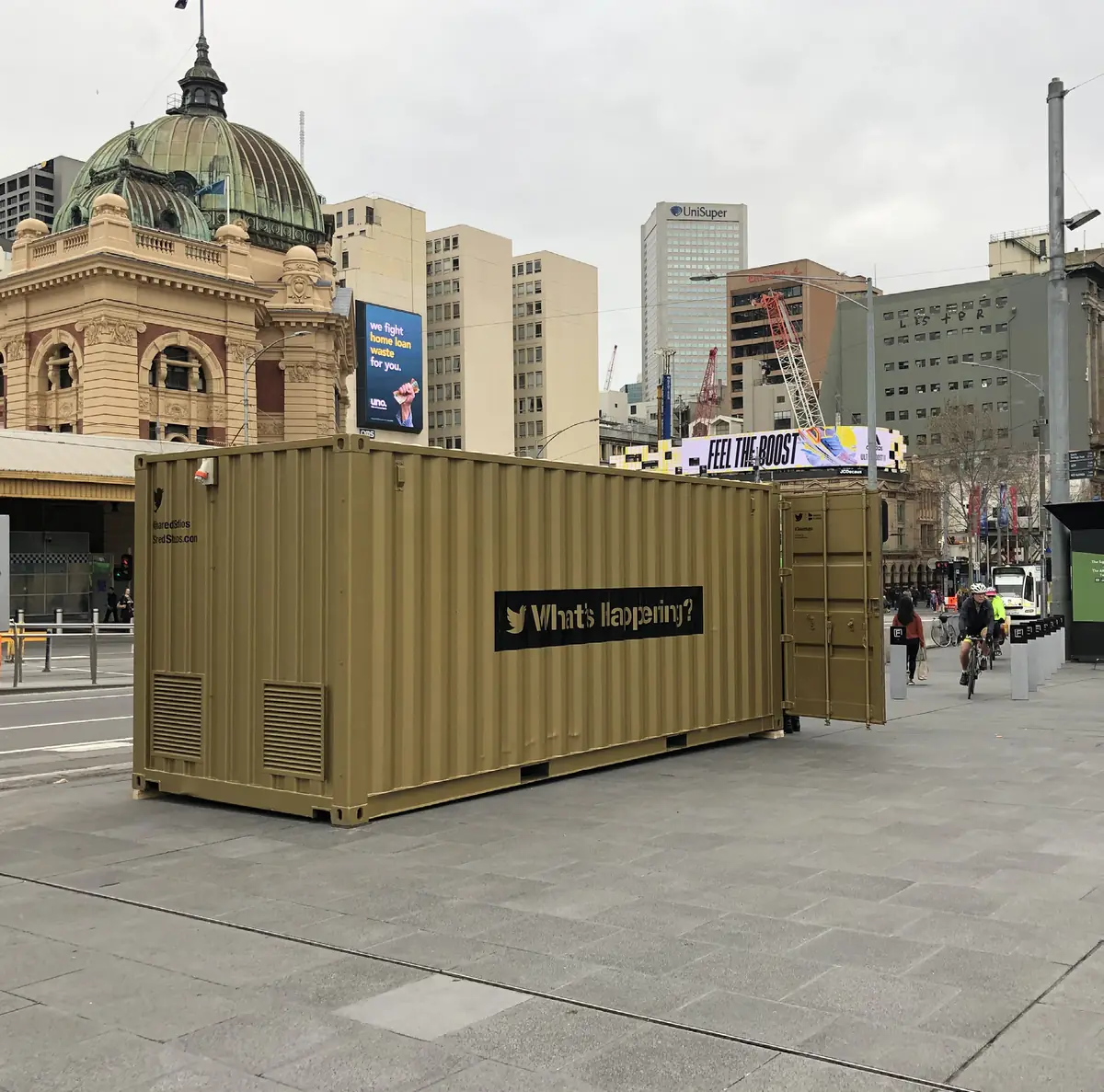 The gold Shared Studios portal container at Federation Square, carrying a Twitter What's happening? sign, opposite Flinders Street Station.